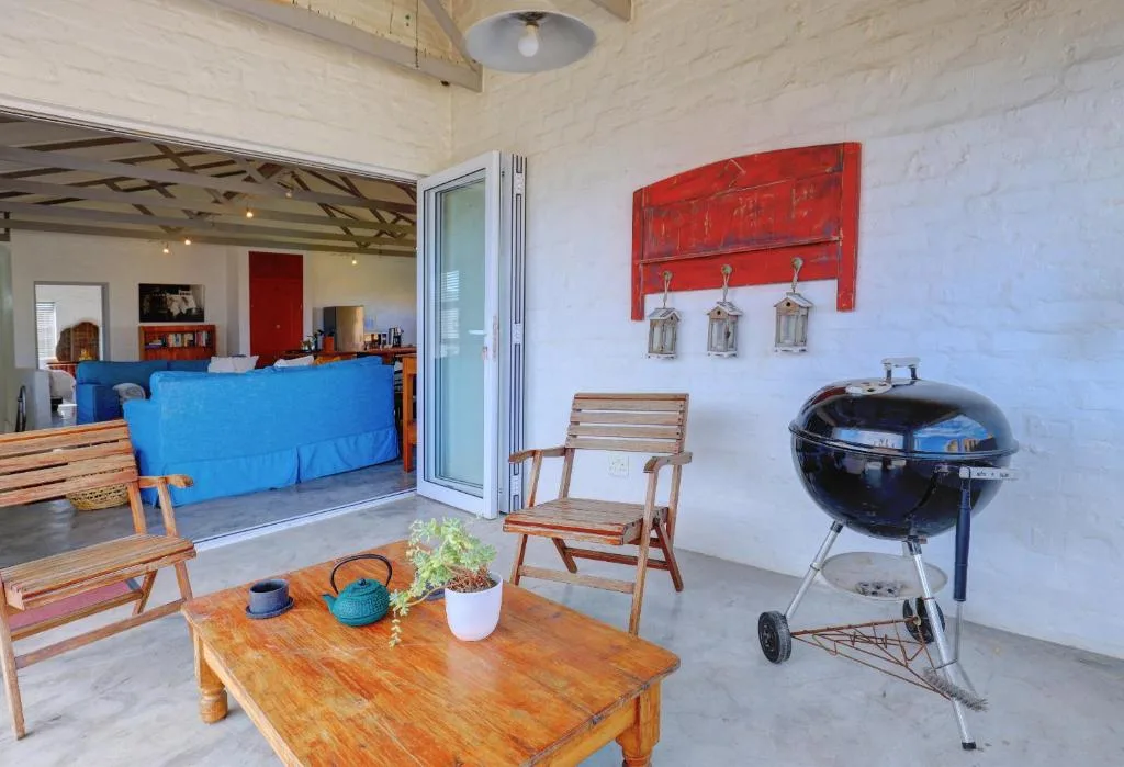 Covered outdoor braai area with wooden furniture and black kettle grill