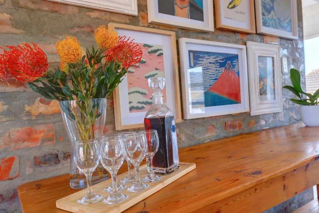 Fresh protea flowers in vase with wine glasses and decanter on wooden shelf