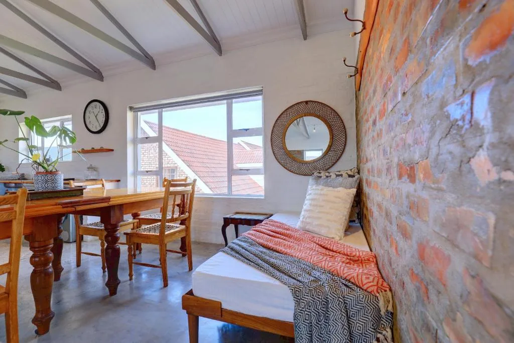 Open-plan interior showing dining table, bed, and exposed brick wall decor