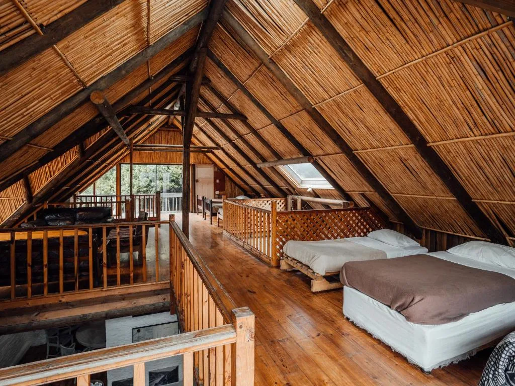 Spacious loft bedroom with two beds, wooden beams and thatch ceiling