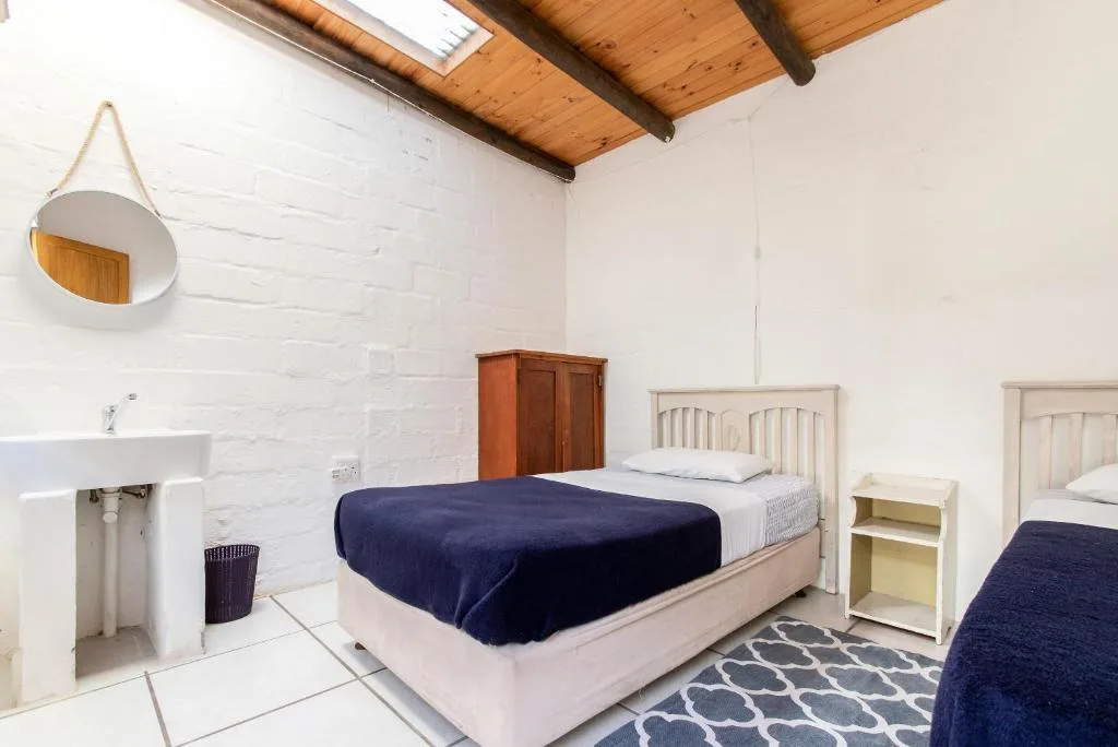 Bright bedroom with two beds, wooden beams, and en-suite sink area
