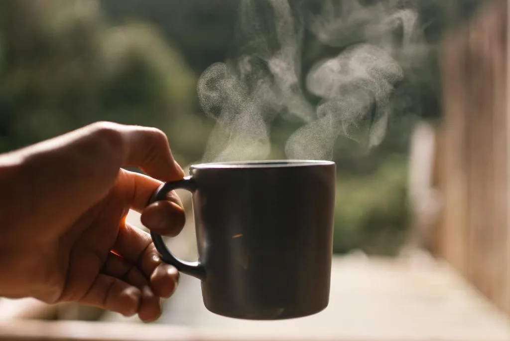 Steaming mug held in hand with garden view backdrop
