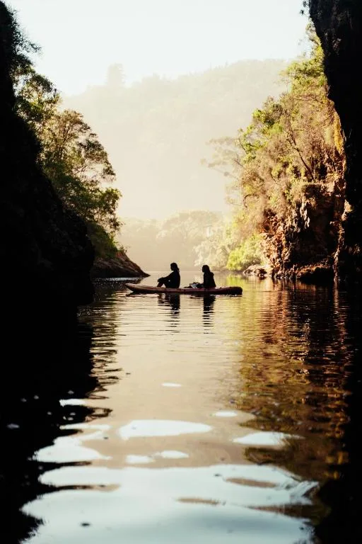 People kayaking on serene river between lush green cliffs at sunrise