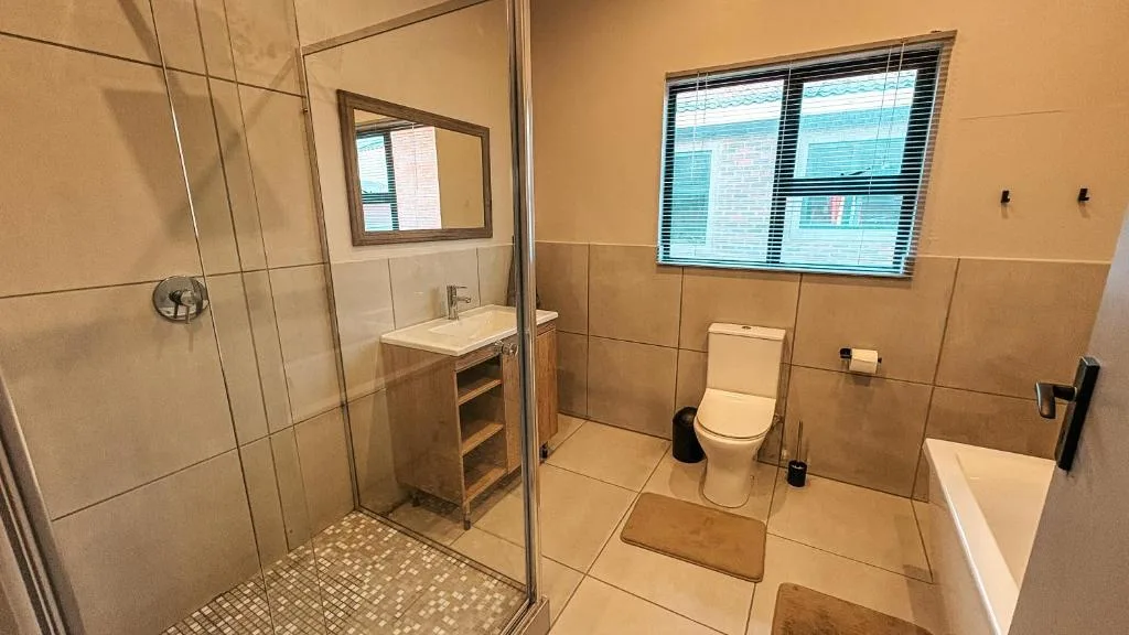 Modern bathroom with walk-in shower, vanity, toilet, and window