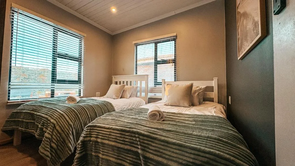 Twin bedroom with striped bedding, white headboards, and large windows