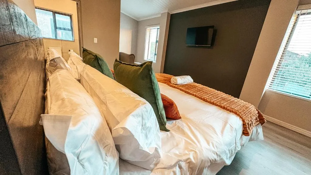 Spacious bedroom with twin beds, green accent wall, and wall-mounted TV