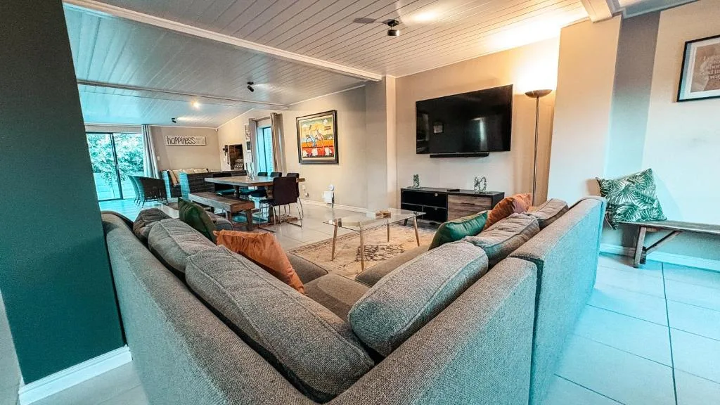 Open-plan lounge with grey sectional sofa, wall-mounted TV, and dining area