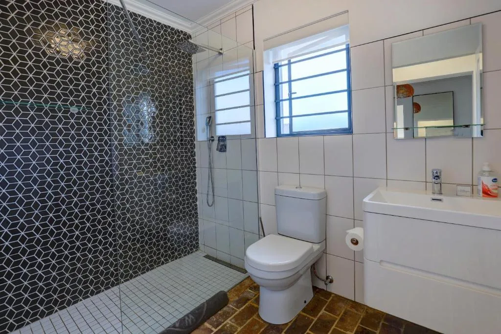 Modern bathroom with geometric tiled shower, white vanity, and toilet