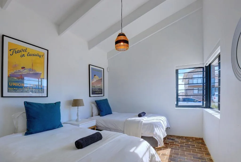 Bright bedroom with twin beds, blue cushions, vintage travel posters, pendant light