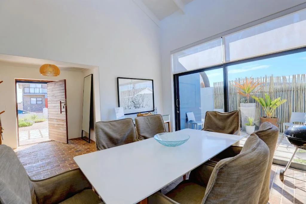 Modern dining area with white table and upholstered chairs overlooking deck