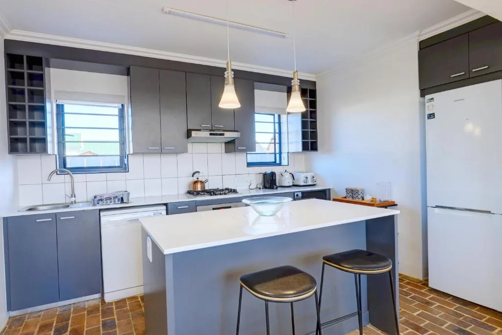 Modern kitchen with dark cabinetry, white counters, island seating, and stainless appliances
