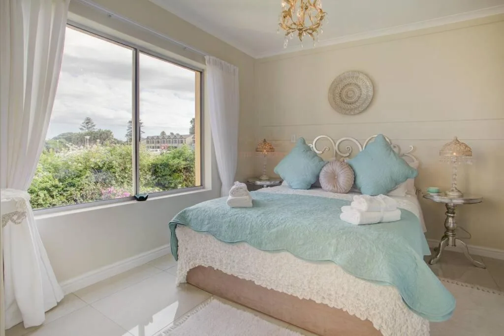 Bright bedroom with turquoise bedding, ornate headboard, and large windows overlooking garden