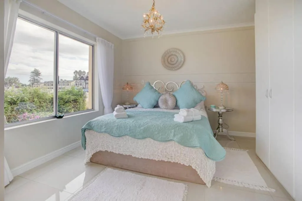 Elegantly styled bedroom with turquoise bedding and decorative pillows, garden view through large window