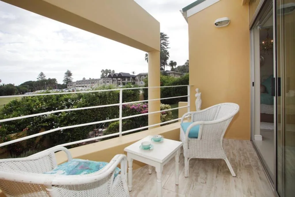 Spacious balcony with white wicker seating and sea view overlooking gardens