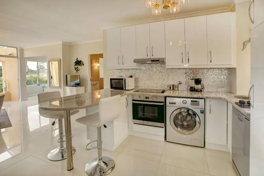 Modern white kitchen with granite countertop, integrated appliances, and breakfast bar seating