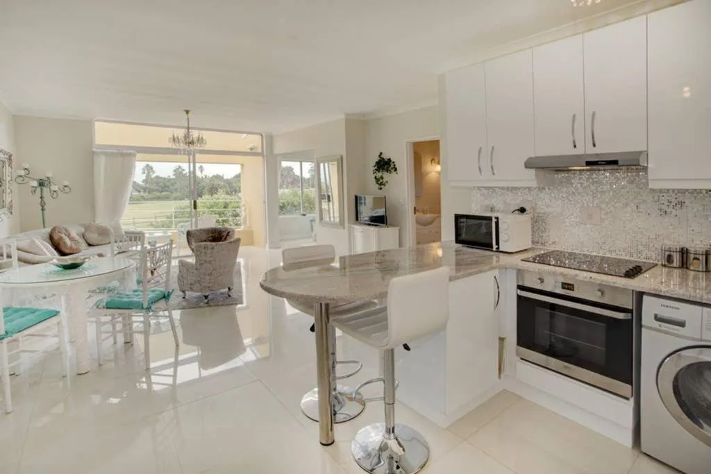 Modern white kitchen with island, stainless appliances, and garden views
