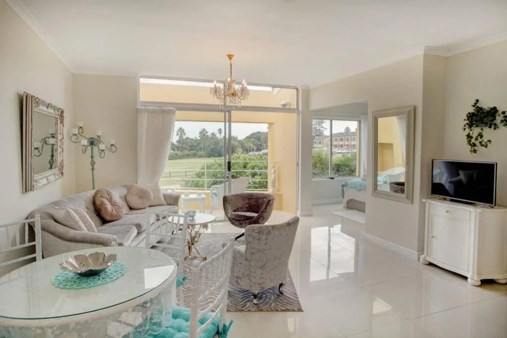 Bright lounge with sofa, armchairs, TV, and large windows overlooking gardens