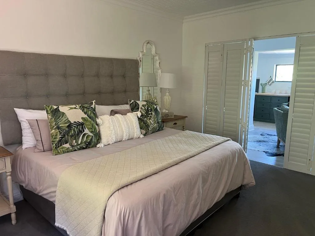 Modern bedroom with upholstered headboard, tropical patterned pillows, and ensuite access