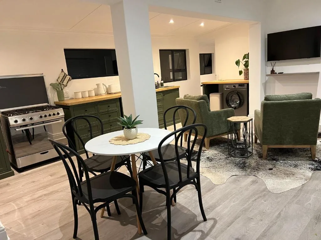 Open-plan dining area with round white table and black chairs facing kitchen