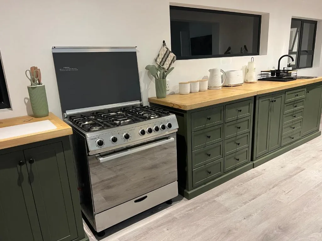 Modern kitchen with gas stove, green cabinetry, wooden countertops, and large mirror