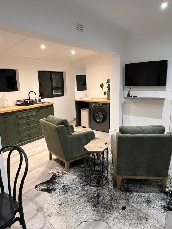Open-plan lounge with green armchairs, TV, kitchen, and washing machine visible