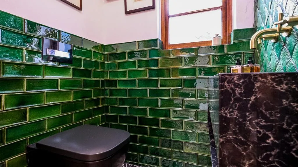 Modern bathroom with striking green subway tile walls and dark toilet