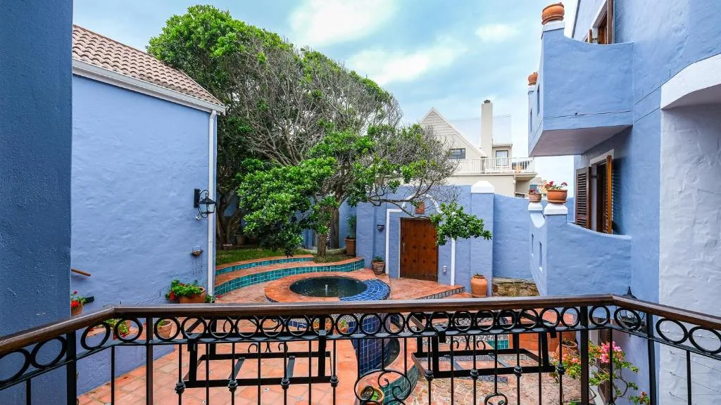 Ornate black railing overlooking courtyard with blue walls and mature tree