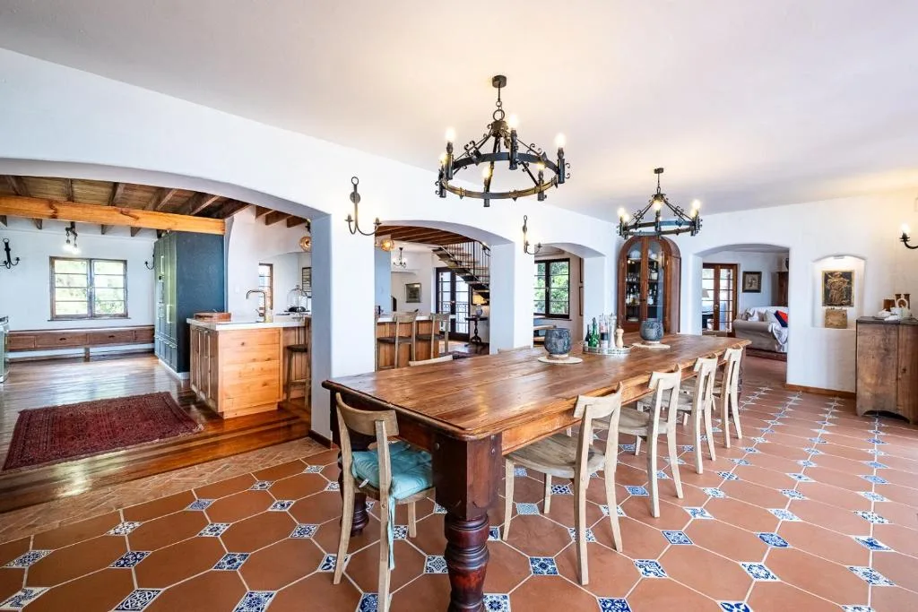 Spacious dining room with wooden table, decorative chandeliers, and terracotta tiled floor