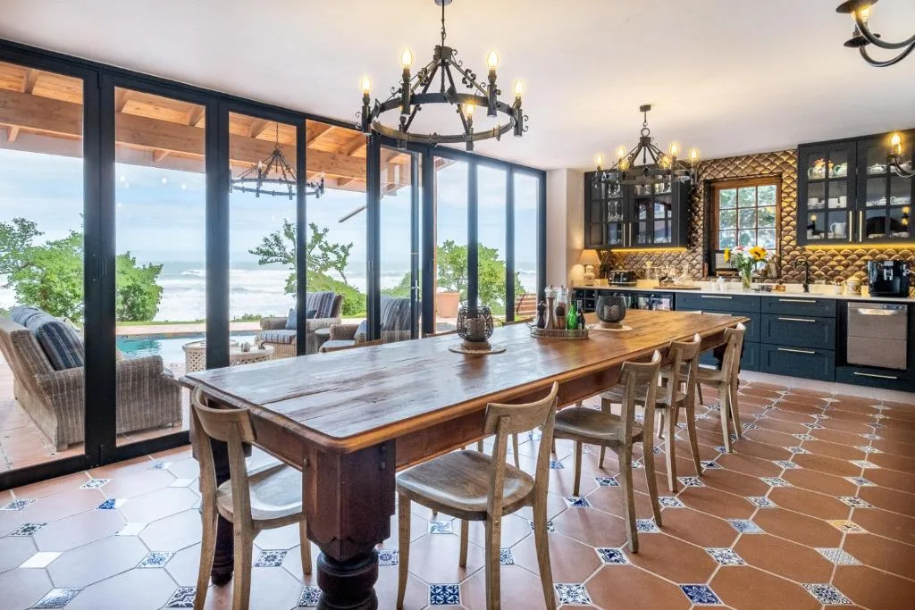 Spacious dining area with wooden table, ocean view through floor-to-ceiling windows