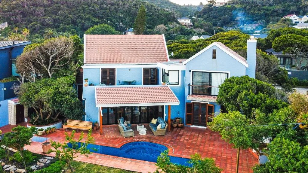 Blue villa with red-tiled roofs and swimming pool surrounded by lush gardens