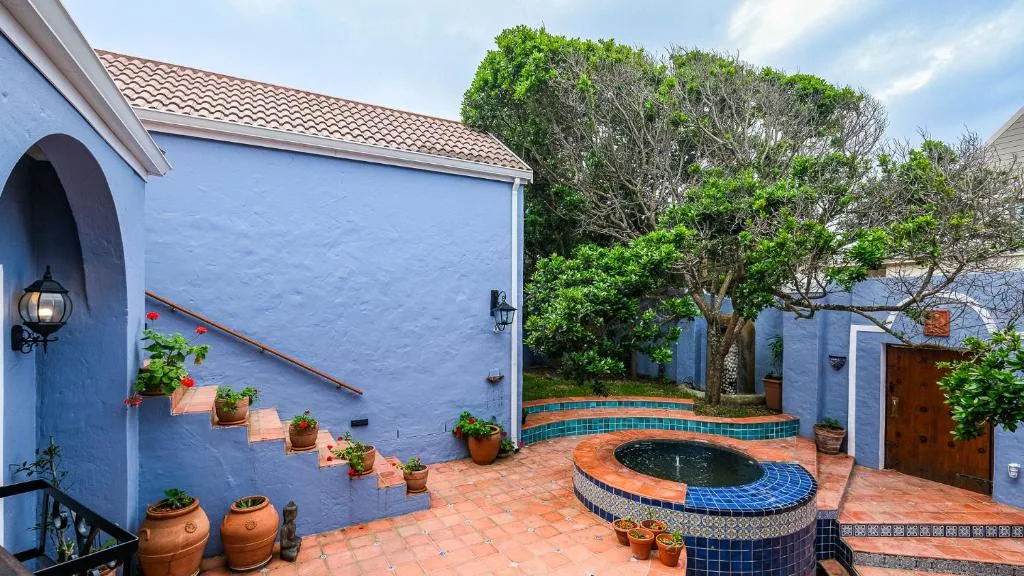Bright blue villa exterior with terracotta courtyard, potted plants, and decorative water feature