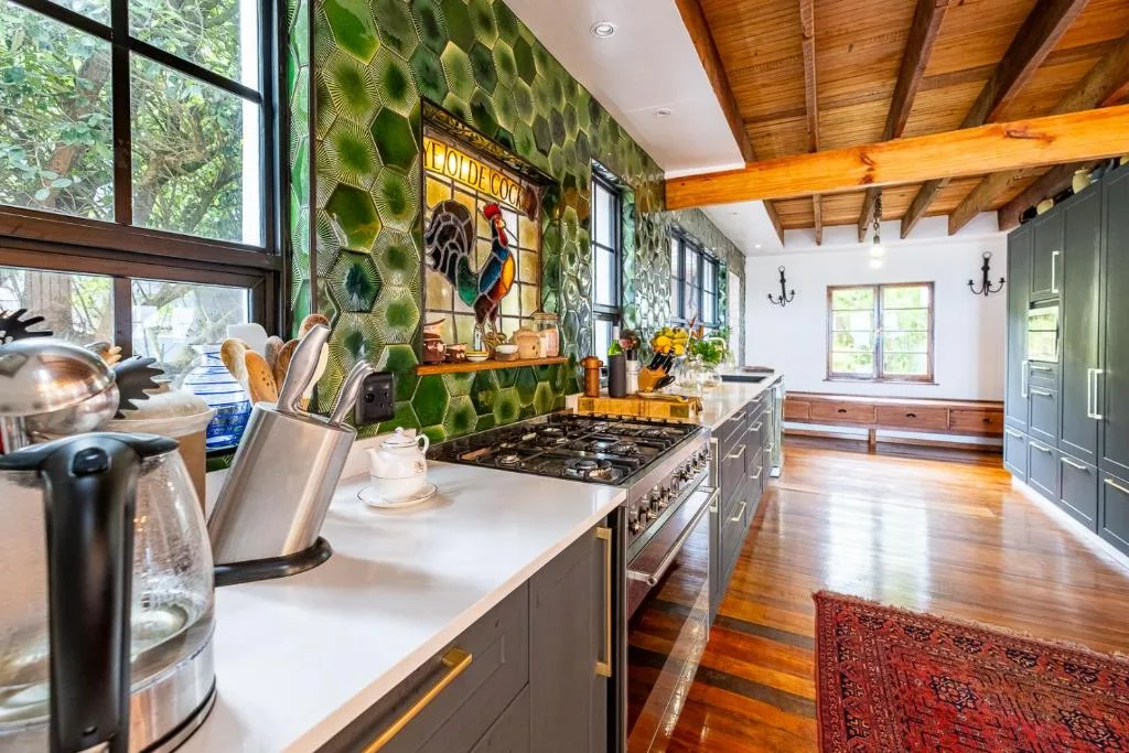 Modern kitchen with green patterned walls, gas range, wooden beams, and stainless steel appliances