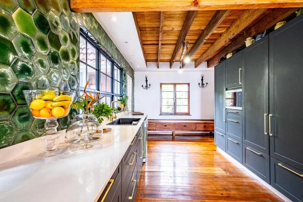 Modern kitchen with green patterned wallpaper, white countertop, dark cabinetry, wooden beams