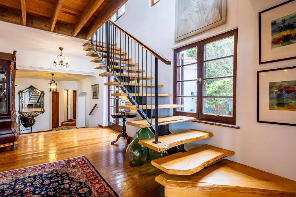 Spacious open-plan lounge with wooden staircase, polished floors, and artwork