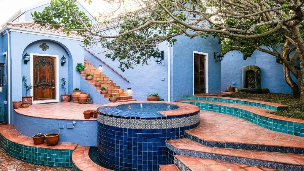 Blue-tiled circular hot tub in charming courtyard with terracotta paving and mature tree