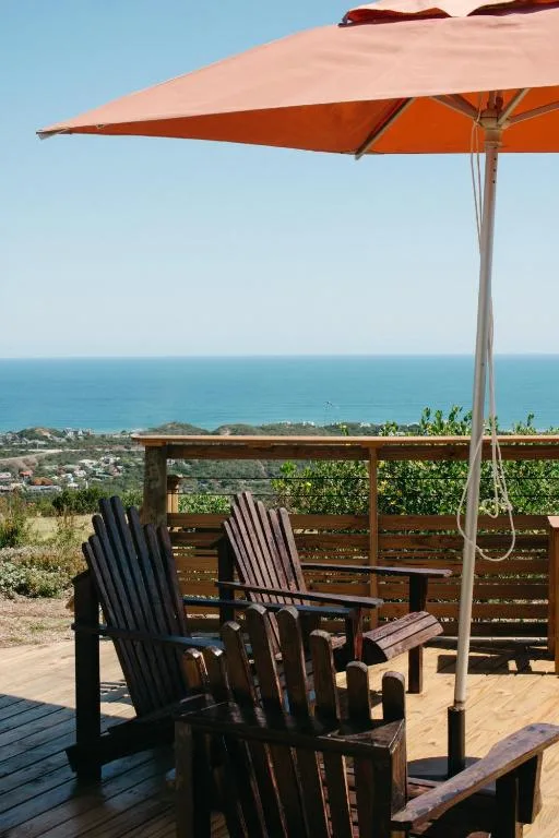 Wooden deck with Adirondack chairs and orange parasol overlooking ocean