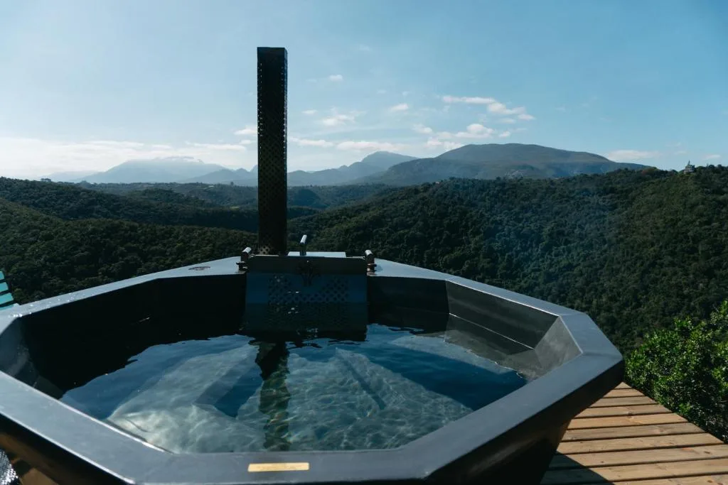 Modern hexagonal hot tub overlooking forested mountains and valley landscape