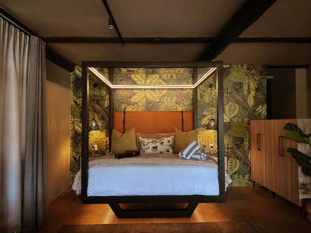 Luxurious four-poster bed with orange headboard and botanical wallpaper accent wall