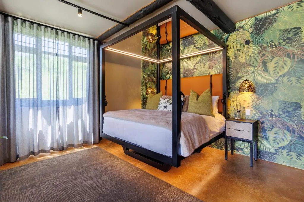Spacious bedroom with black four-poster bed, botanical wallpaper, and large windows