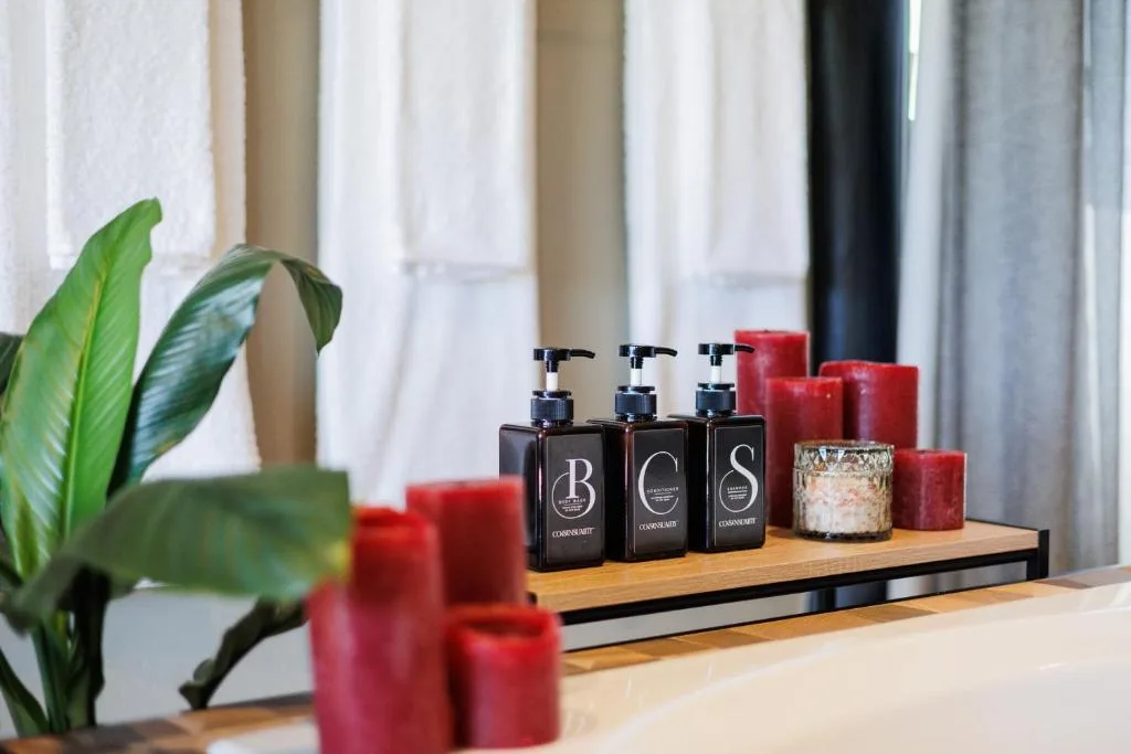 Luxury bathroom amenities with black dispensers, red candles, and potted plant