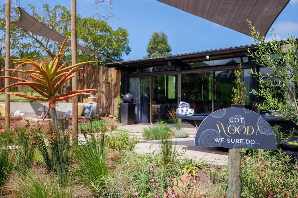 Modern black cabin with large windows, landscaped garden, shade sails, and welcome sign