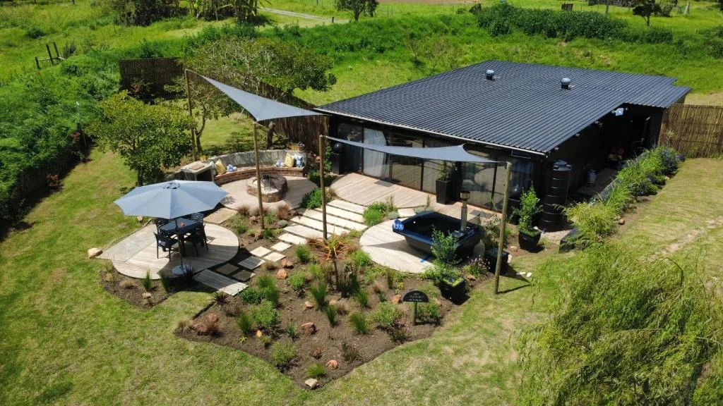 Modern black-roofed cabin with curved deck, umbrellas, and manicured gardens