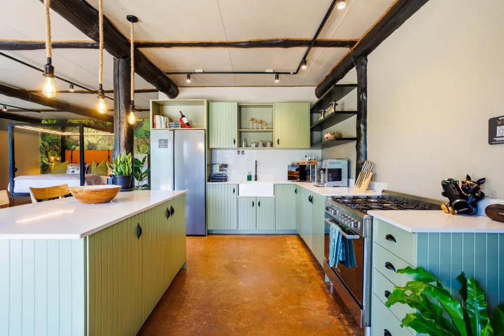 Modern kitchen with sage green cabinetry, stainless steel appliances, and exposed beams