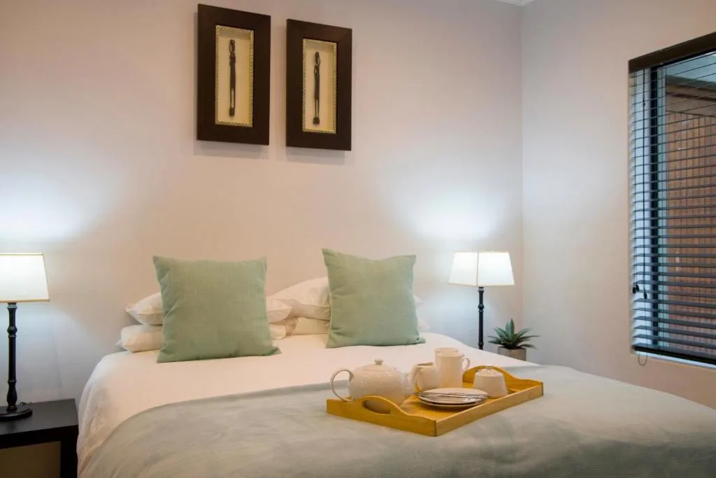 Bright bedroom with white bed, green pillows, bedside lamps, and framed wall art