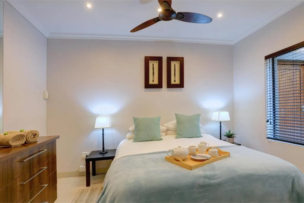 Bright bedroom with queen bed, green cushions, bedside lamps, wooden dresser