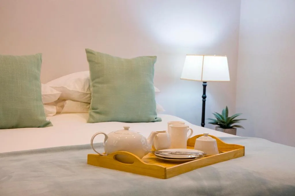 Bright bedroom with green pillows, bed tray with tea service, and lamp