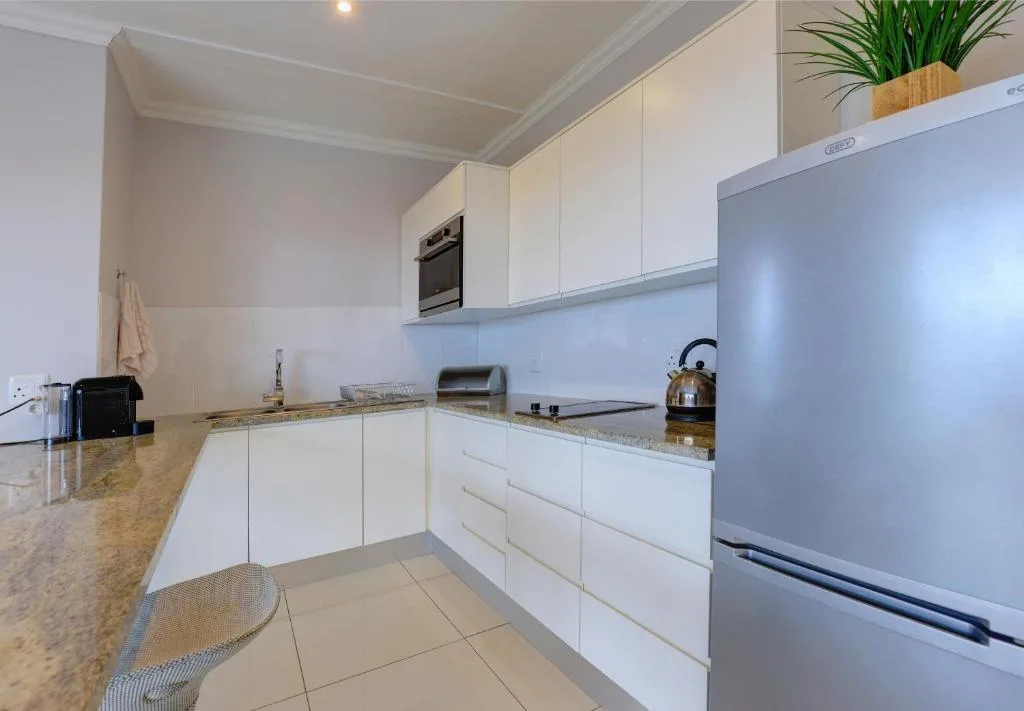 Modern white kitchen with granite counters, stainless steel appliances, and built-in oven