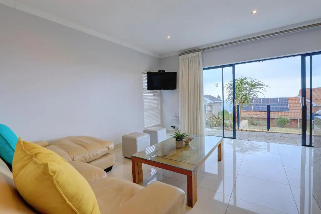 Bright lounge with cream sofa, yellow pillows, wall-mounted TV, and large windows overlooking garden