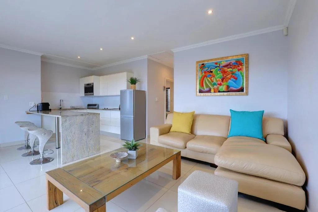 Open-plan lounge with beige sofa, colorful artwork, and modern kitchen visible