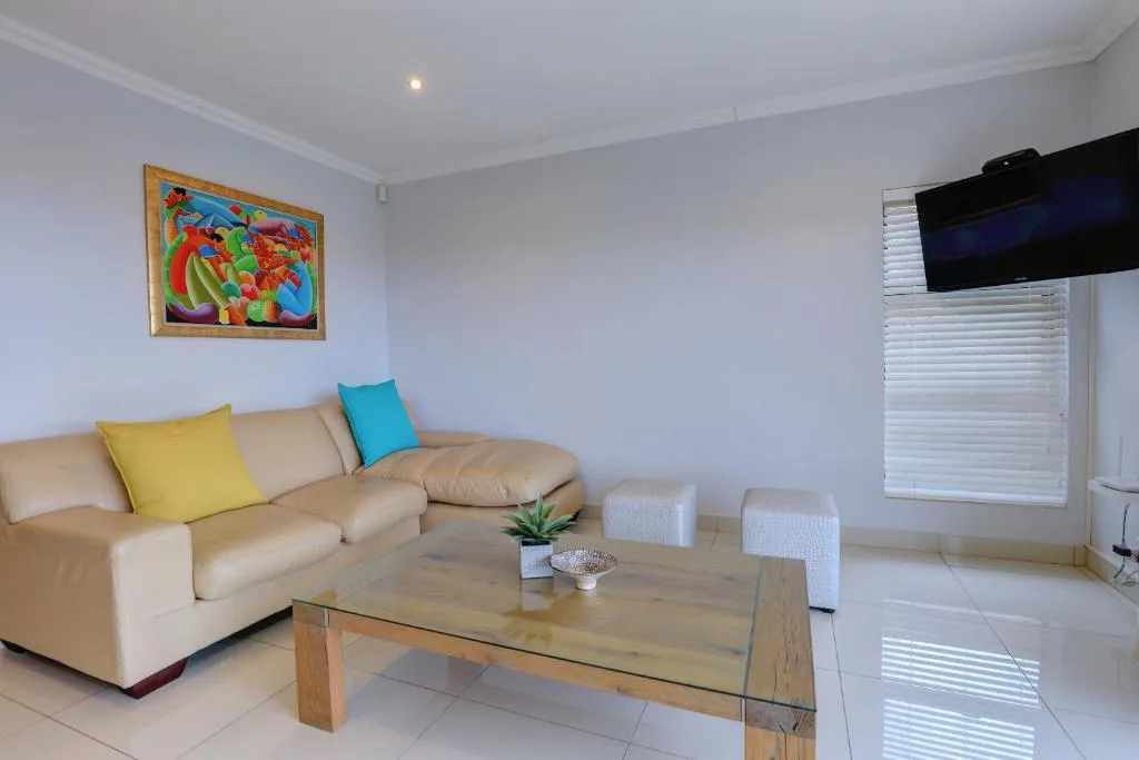 Bright living room with beige sofa, glass coffee table, wall art, and television